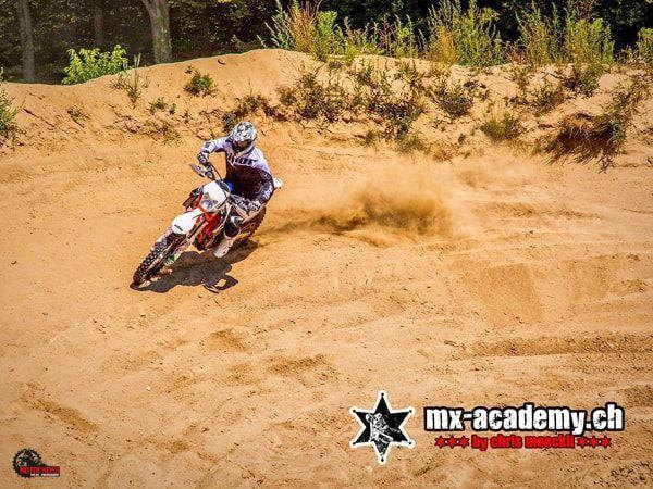 Action sports in a sandy corner: the rear wheel of the motocross bike throws up a wide fountain of sand