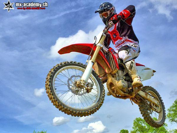 Adrenaline sports seen from below: a rider on a red Honda jumps against a cloudy sky