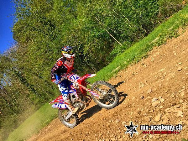 Adventure on a dirt slope: Honda rider with the front wheel in the air, surrounded by trees