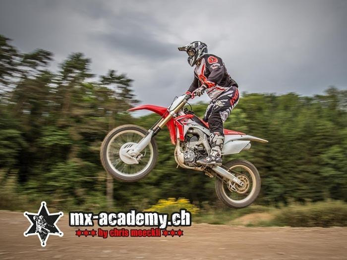 BMX technique on a motocross bike: a rider jumps over a crest in front of a row of trees