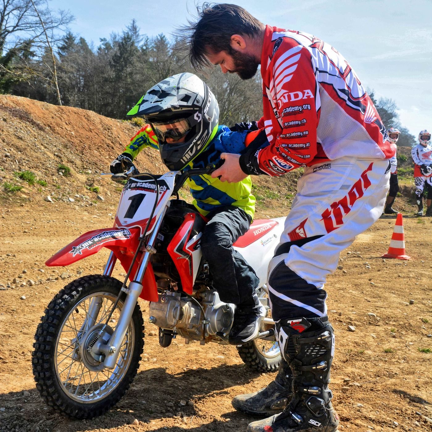 Children's dirt bike with coach: kneeling at eye level, the coach explains something to the child on the bike