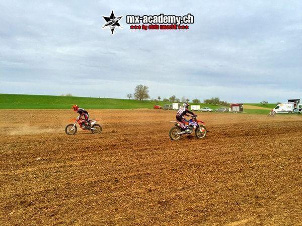 Company outing with motocross: two riders on a wide expanse of dirt, parked vehicles behind them