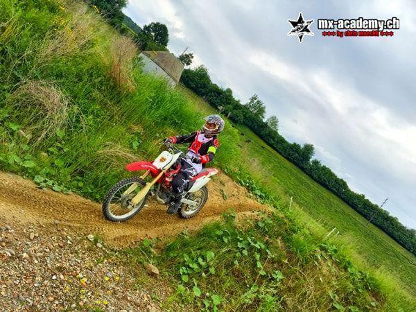 Dirt bike course on a slope: a red Honda rides along an earth path on green terrain, tilted camera angle