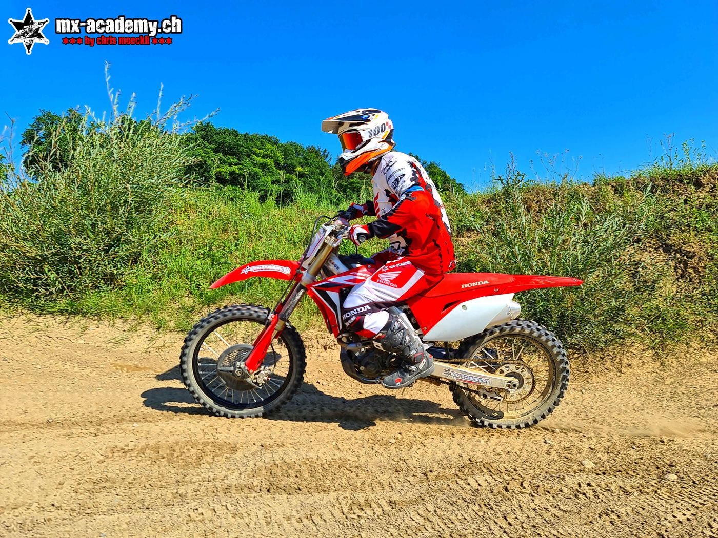 Dirt bike hire: a rider on a red Honda CRF crosses the sandy track, with blue sky above him