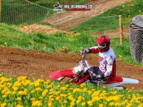 Dirt bike in a corner: rider in a red helmet, with yellow dandelions glowing in the foreground