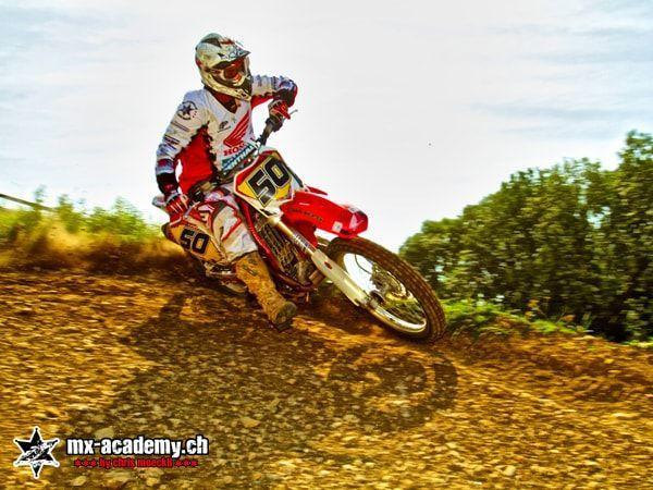 Dirt bike leaning into a turn: rider with race number 50 banks into the corner, trees behind
