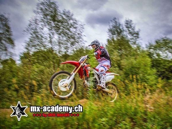 Dirt bike track: a red Honda takes off over the meadow, the picture looks blurred from the motion
