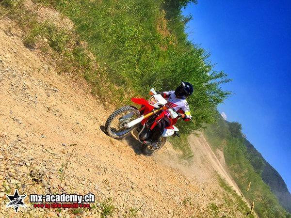 Downhill and motocross: rider on a red Honda on a steep dirt slope, shot from an oblique perspective