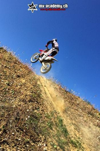 Downhill riding with a difference: motocross rider powering up a steep slope, blue sky above him
