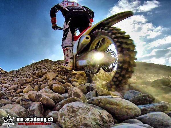 Enduro bike from a worm's-eye view: a rider with race number 50 rolls over large round stones