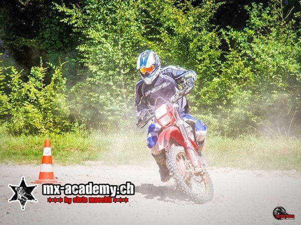 Enduro photos: rider in a blue jacket at the cone, dust and green bushes behind him