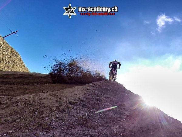 Extreme sports against the light: a rider on a motocross bike at the top of a crest, dirt spraying all around
