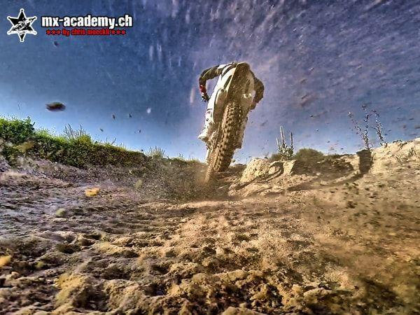 Extreme sports from a worm's-eye view: a motocross rider from behind, churned-up dirt flying towards the camera