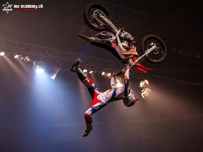 FMX tricks indoors: a freestyle motocross rider hangs high above the ground during a trick