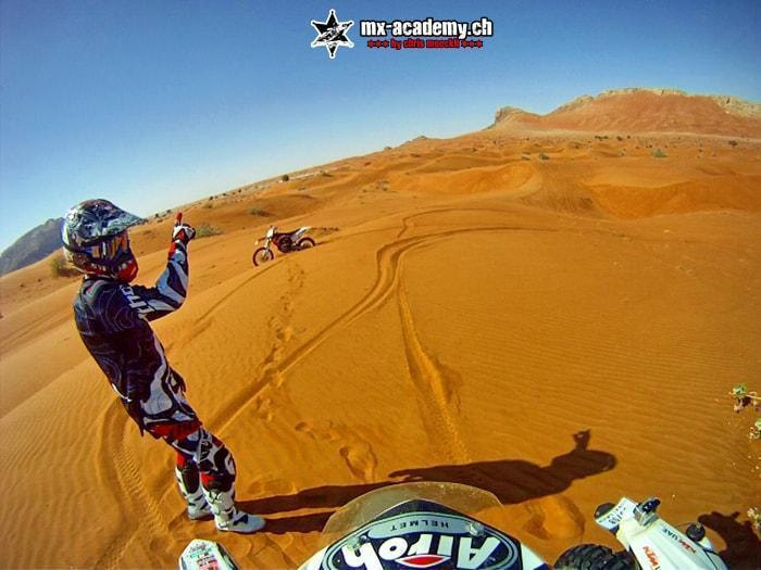 Freeride extreme in the desert: a rider raises one arm in the air in front of the sand dunes