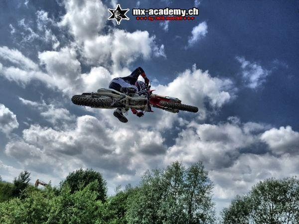 Freestyle motocross style sideways jump: the rider tilts the bike, with a cloudy sky above