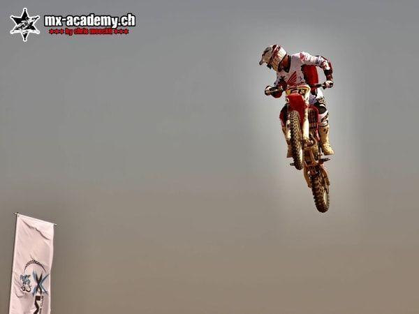 Frequently asked motocross questions: a rider jumps high under a grey sky, a flag at the bottom left