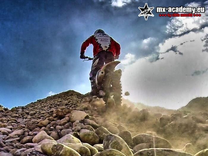 Hard enduro over boulders: an enduro rider rides over large rocks while dust swirls up behind him