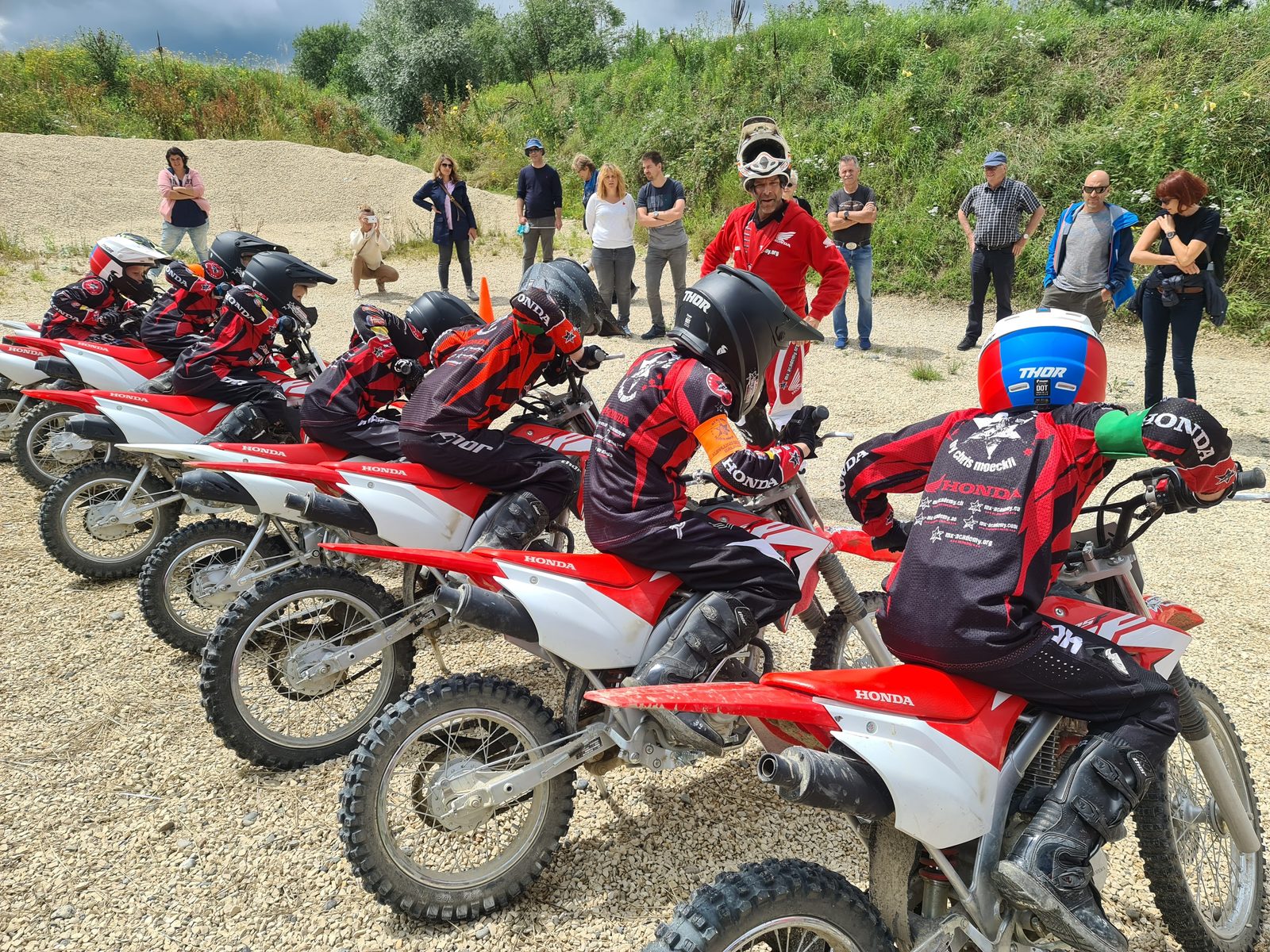 Kids motocross in a group: children on Honda CRF bikes, with their parents standing next to them