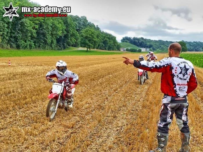 Kids motocross lessons: a child on a kids' motorbike while the coach points out where to ride