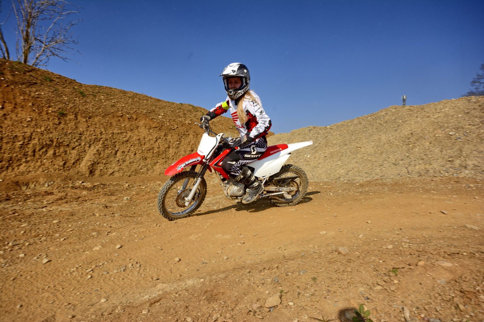 Learning motocross: a rider takes a Honda over a sandy hill, with blue sky above