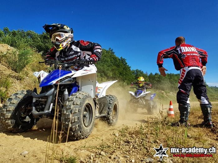 Mini quad riding: a child sits on a small quad out in the terrain, with a coach standing beside him