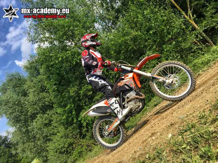 Motocross adventure in the woods: rider tackles a steep stretch of slope between the trees on his bike