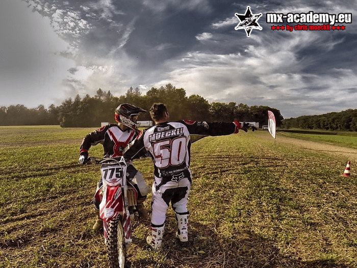 Motocross club training: riders and coach point towards the track with outstretched arms