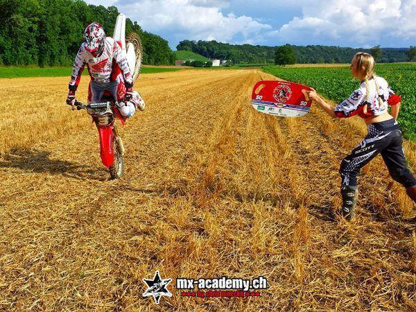 Motocross courses: a rider balances the Honda on its front wheel while a helper holds up a board showing 50