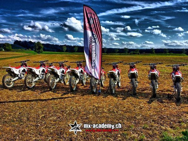 Motocross events calendar: Honda motorbikes in a row beside the MX-Academy flag, with clouds overhead