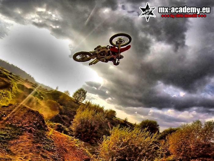 Motocross FAQ at the MX-Academy: a rider in mid-jump against a dark thunderstorm sky