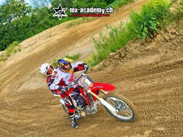 Motocross lessons: two riders together on a red Honda with race number 1 in a banked corner during the course