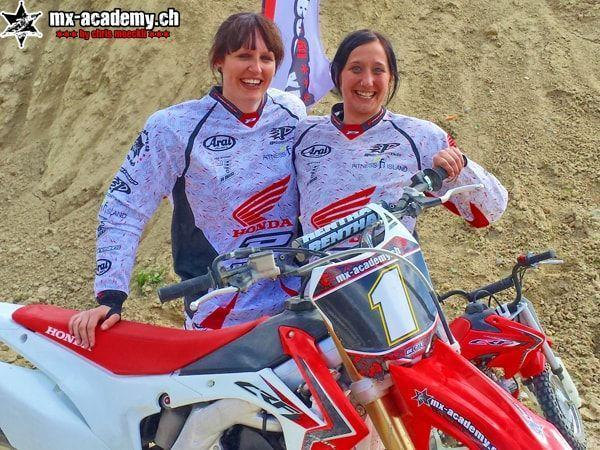Motocross photos: two smiling female riders in Honda jerseys by a Honda with number 1