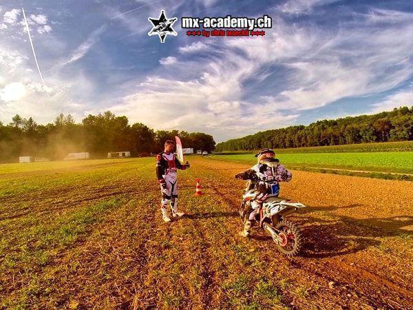 Motocross pictures: helper holds up a board, a rider waits at the cone for the signal