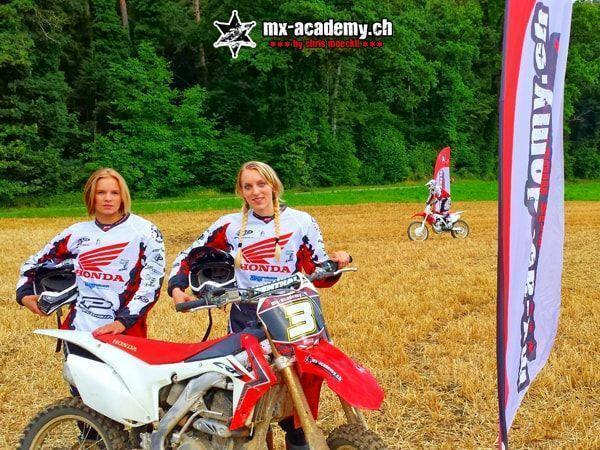 Motocross pictures: two female riders in Honda jerseys, helmets in hand, next to a Honda