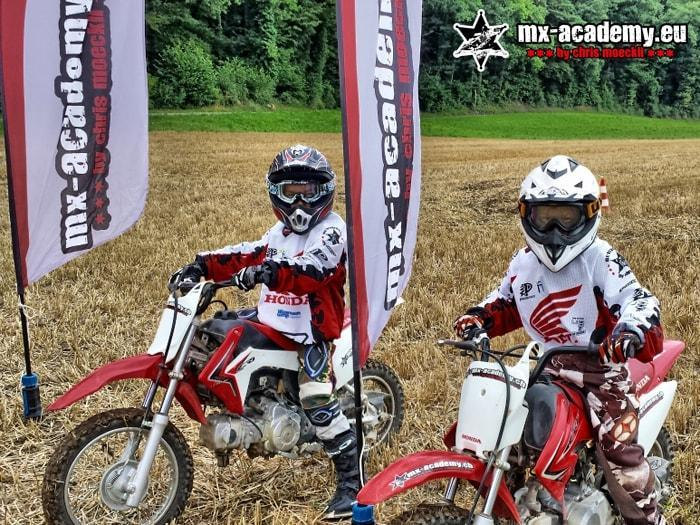 Motocross questions about kids motocross: two young riders sit on their kids' bikes in front of the flags