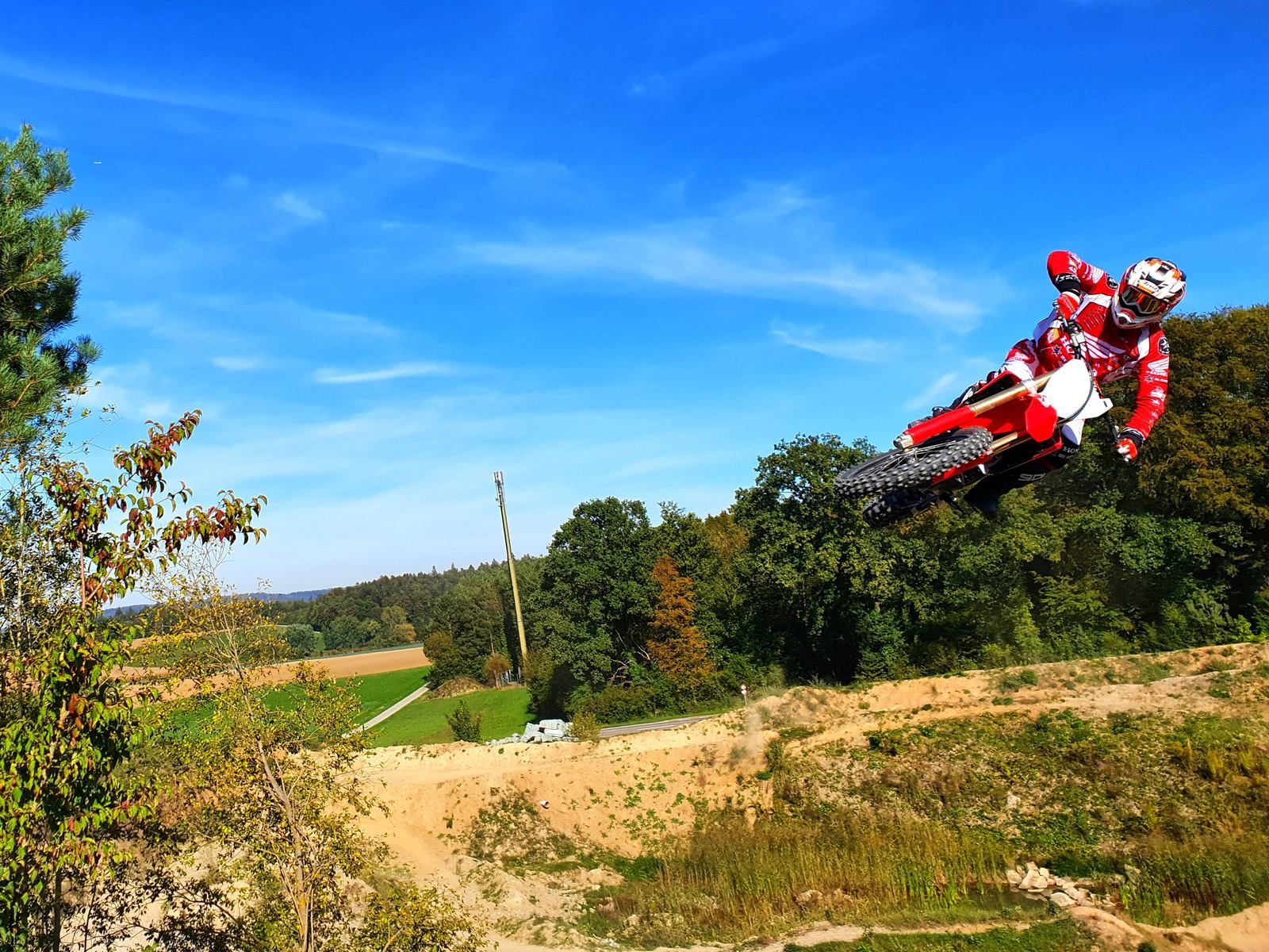 Motocross school MX-Academy: rider jumping against a blue sky above green countryside