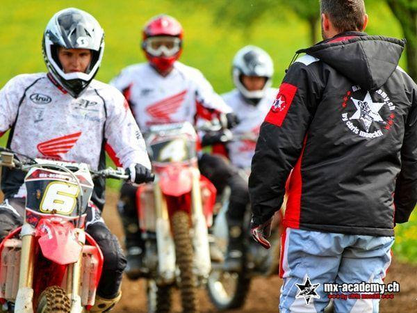 Motocross trainer in an MX-Academy jacket briefing three attentive riders in Honda jerseys