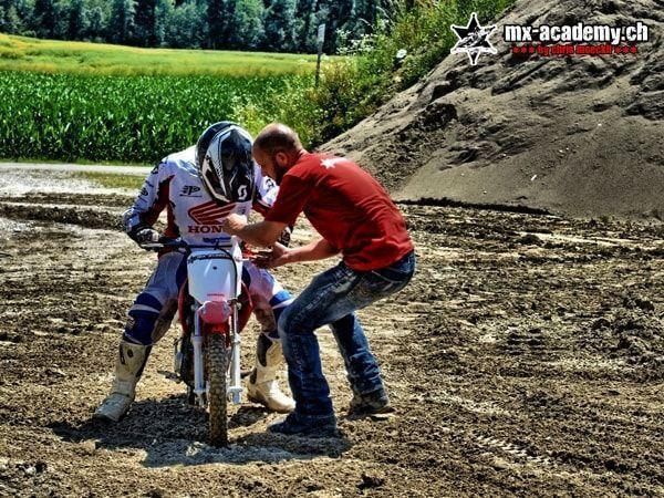 Motocross videos from beginner training: coach in a red T-shirt helps a rider on a Honda in the mud