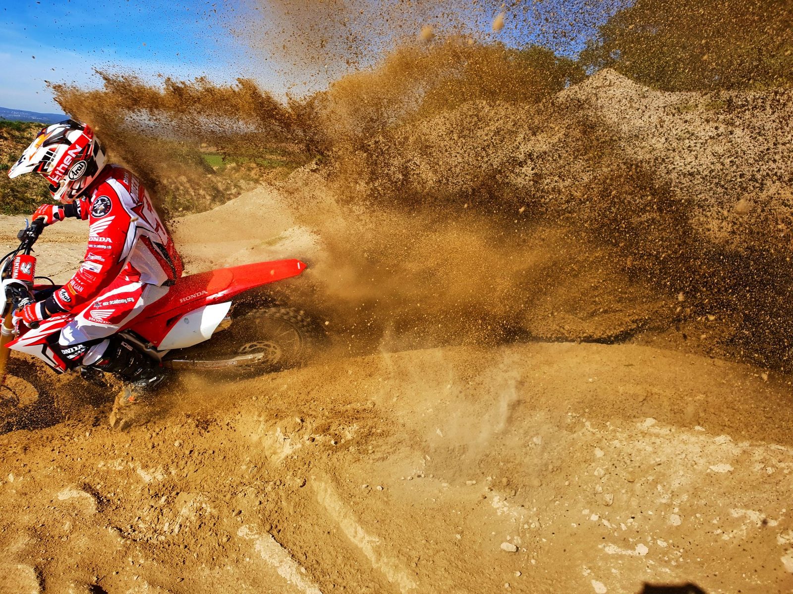 Motorcycle cornering training in sand: a high fountain of sand sprays up behind the motocross rider in the corner