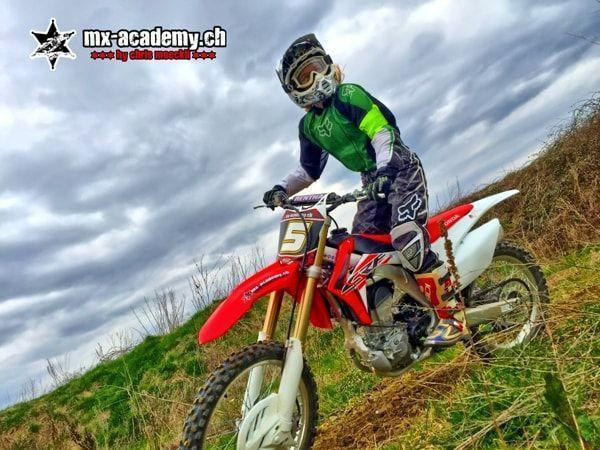 Motorcycle off-road: female rider in a green jersey with race number 5 on her Honda on a grassy slope