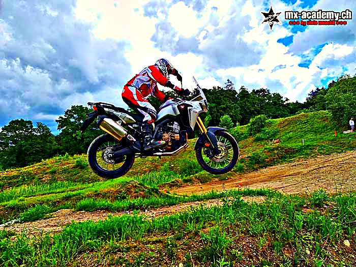 Motorcycle safety training: a Honda Africa Twin takes off over a dirt mound on off-road terrain