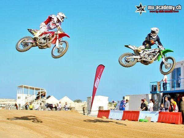 Motorsport experience: two motocross riders in the air at the same time, spectators and a grandstand below