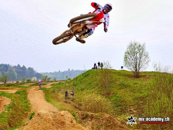 Motorsport up close: motocross rider flies far across the track, spectators stand on the green hill above
