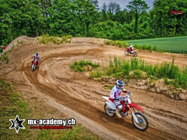 Motorsport weekend on sand: three motocross riders on a winding track between meadow and forest edge