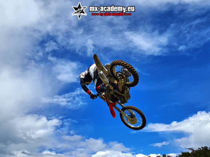 MX club jump: a rider flies through the air on his bike, with blue sky behind him