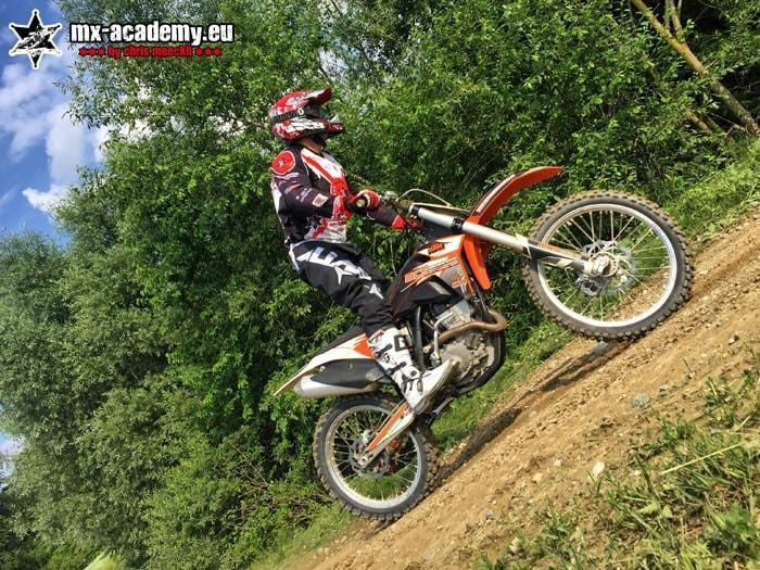 MX team riding technique off-road: motocross rider rides up a slope in the woods