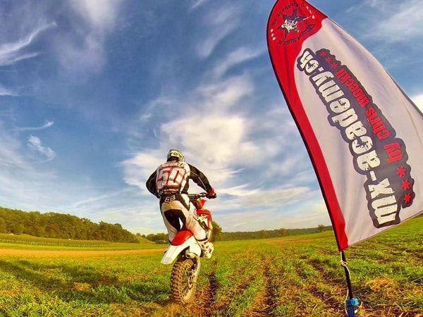 MX track: rear view of a rider with number 50 on a meadow next to the MX-Academy flag