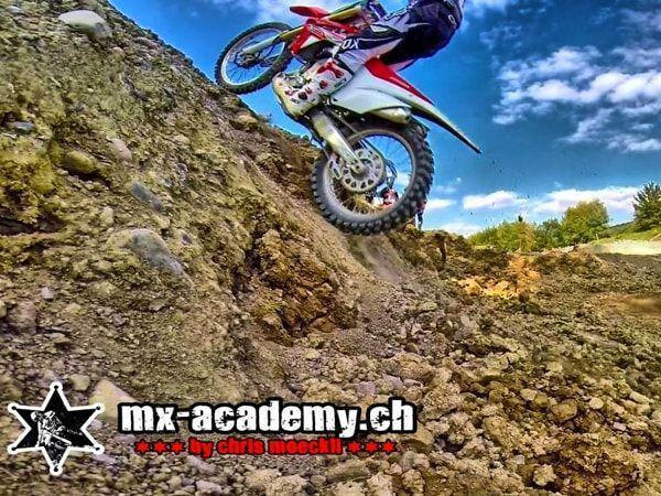 Off-road training on a slope: rider on a steep, stony hillside under a blue sky with clouds