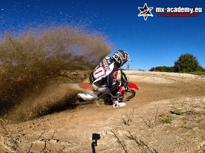 Rent a motocross bike and ride: a rider throws up a high fountain of sand on the track